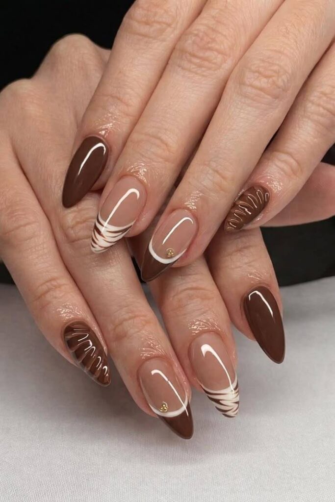 Elegant almond-shaped nails featuring chocolate brown French tips, glossy nude bases, and delicate swirl accents for a classy and modern nail art design.