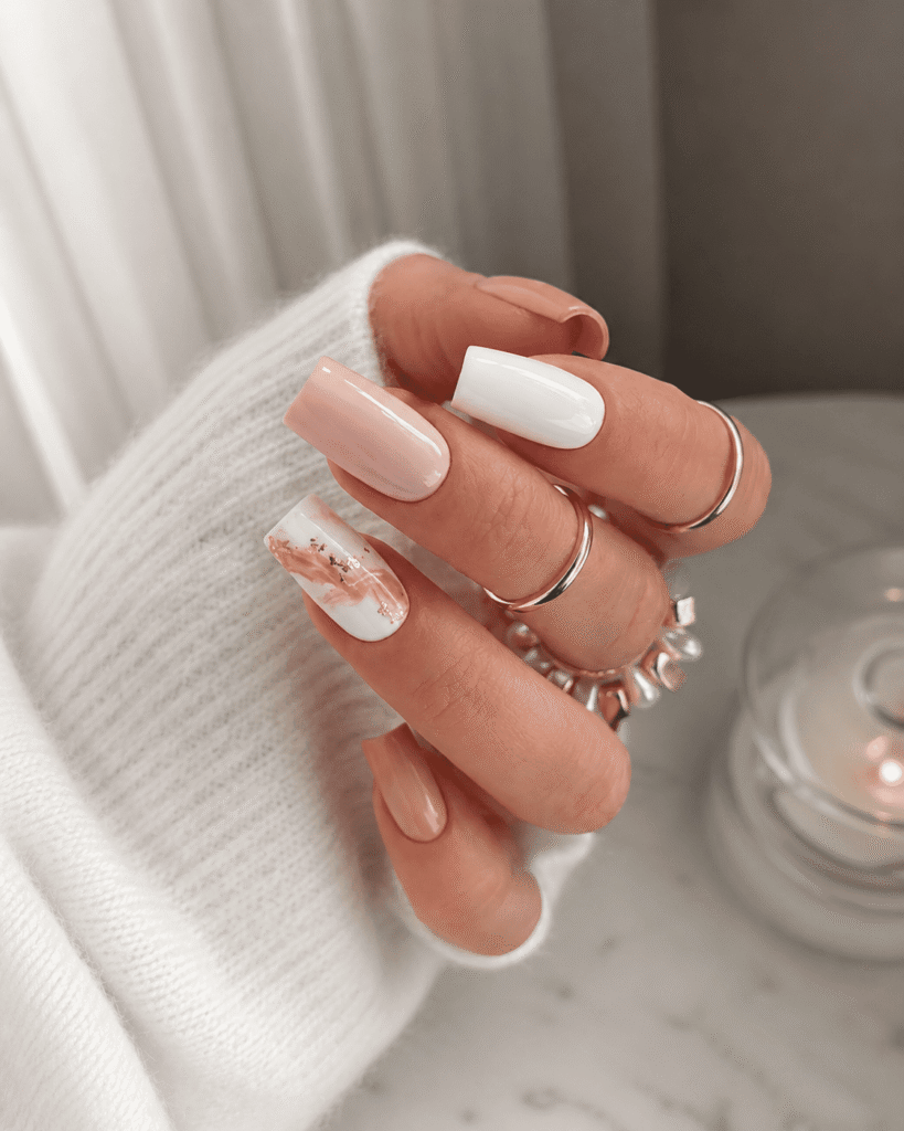 Glossy soft pink and white acrylic coffin nails with elegant marble nail art and gold foil accents, styled with delicate gold rings and a cozy white sweater for a classy feminine manicure look.