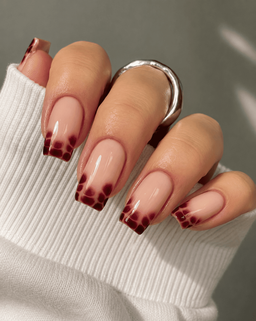 Glossy nude pink nails with deep burgundy tortoiseshell French tips on square-shaped acrylic nails, photographed in soft natural lighting. Elegant luxury nail art design featuring a cozy white sweater sleeve and silver statement ring for a chic fall manicure aesthetic.