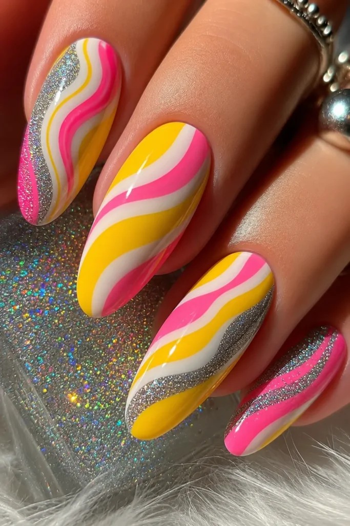 Side-Swooshed Nails Glossy almond-shaped nails with bright yellow, pink, and white swirl nail art accented by silver glitter details. This colorful summer manicure features smooth wave patterns, holographic sparkle, and trendy acrylic nail designs perfect for bright summer nails inspiration.