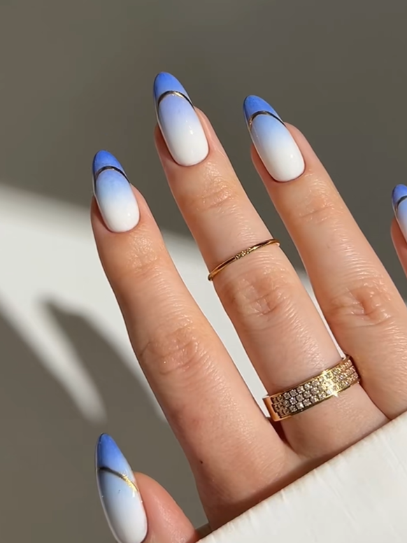 Elegant almond nails with soft pastel blue French tips, white ombré gradients, and delicate gold line accents creating a classy minimalist manicure design.