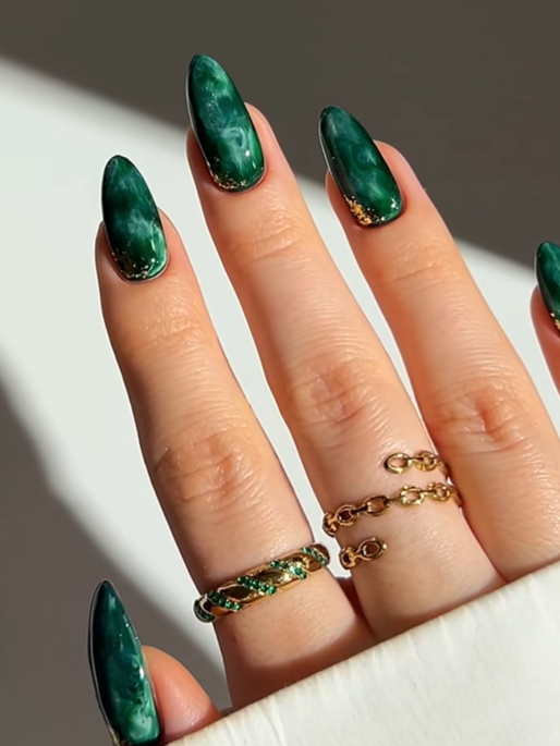 Glossy emerald green almond nails with marble swirl details and subtle gold glitter accents, creating a luxurious and elegant manicure design.