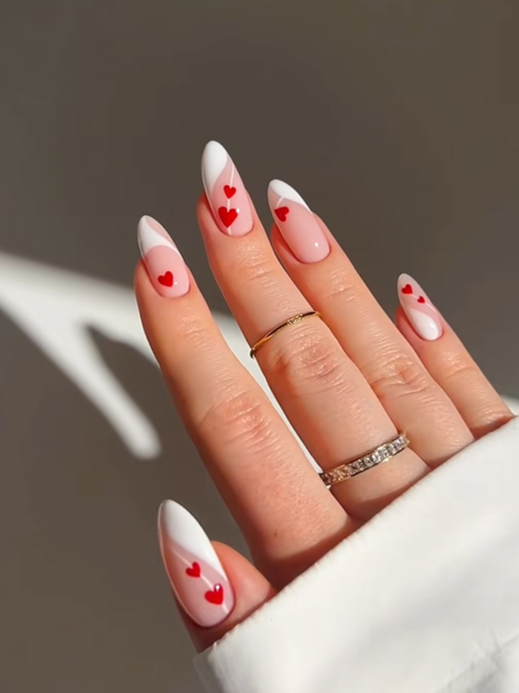 White French tip almond nails with tiny red heart accents on a glossy blush pink base, featuring a chic romantic nail art design perfect for classy manicure inspiration.
