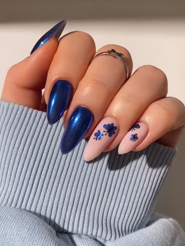 Elegant almond-shaped nails featuring glossy royal blue chrome polish and delicate blue floral nail art on a soft nude base, creating a classy and sophisticated manicure design.