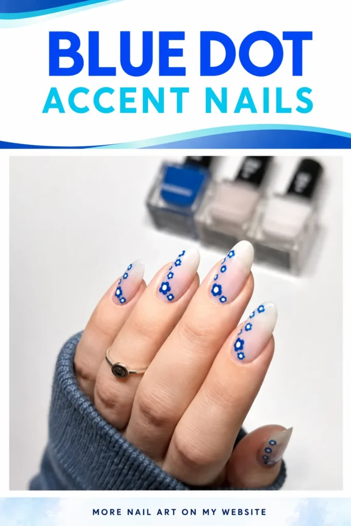 Blue Dot Accent Nails Blue dot accent nails with tiny blue floral patterns on soft white almond-shaped nails, a chic summer nail art idea.